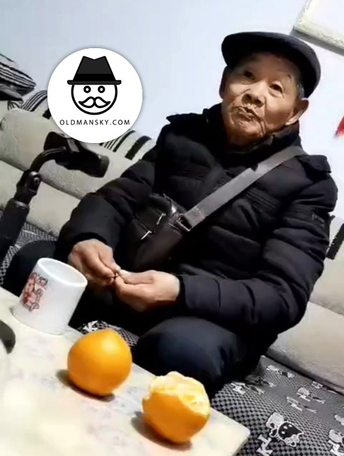 Old man wore black coat and hat ate orange in the living room