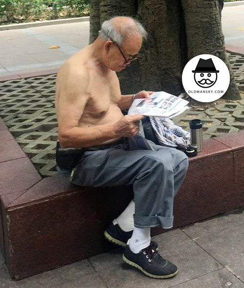 White hair glasses old man wore blue trousers read newspaper under the tree