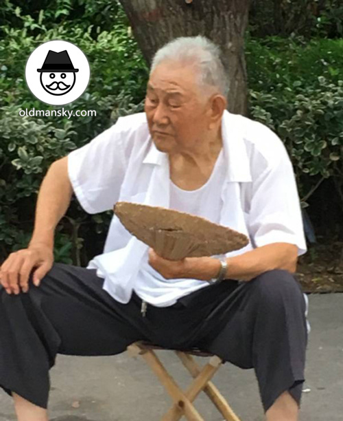 White hair old man wore white shirt sat in the park with a fan