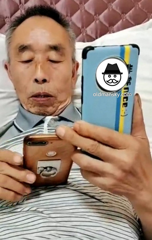 Old man was playing two cellphones in the bed