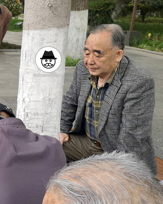 Old man wore plaid gray suit watched people playing Chinese chess