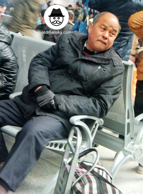 Old daddy wore black coat sat on the chair of railway station