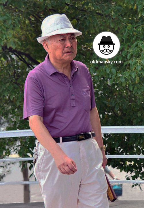 Old man wore purple polo shirt and white trousers walked with a fan