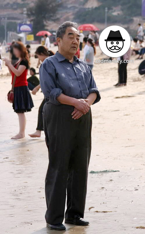 Old man wore brown shirt and black trousers stood on the beach