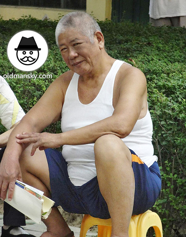 Old daddy wore white vest undershirt and brown middle pants read in the park