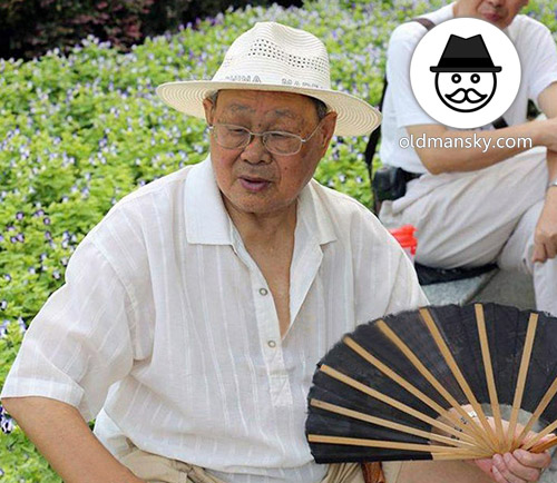 Glasses old man wore a white hat and took a fan rest in the park