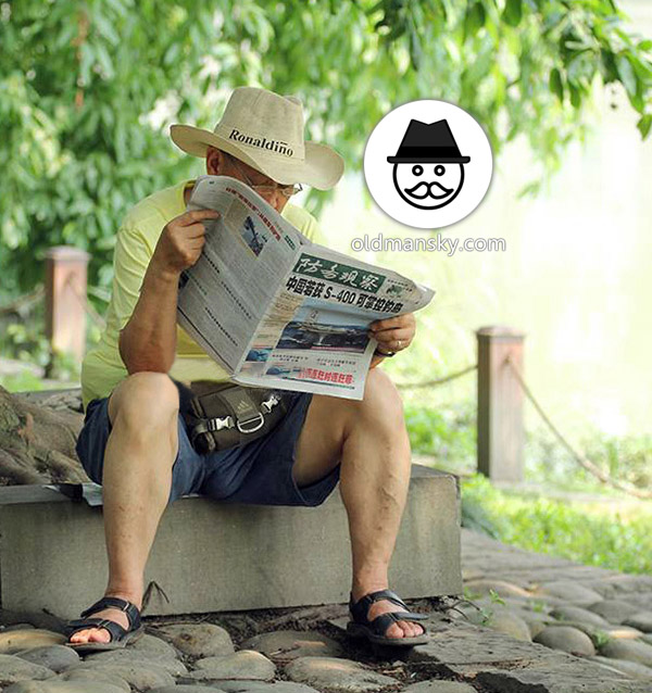 Glasses old daddy wore a yellow t-shirt was reading newspaper by the lake