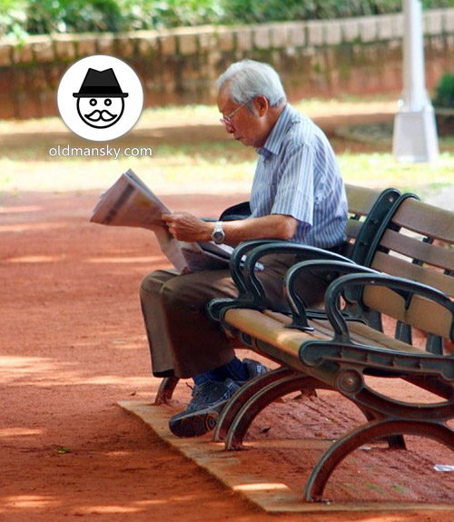 White hair glasses old man was reading newspapers on the park bench