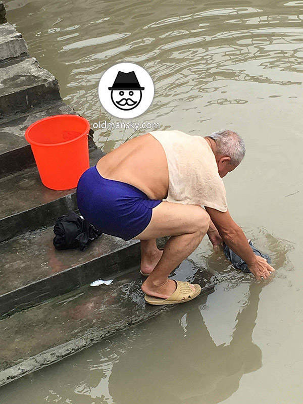 White hair old man wore a brown underwear was washing his head by the river